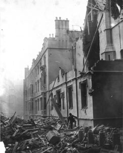 Man in a suit and a bowler hat walking over rubble