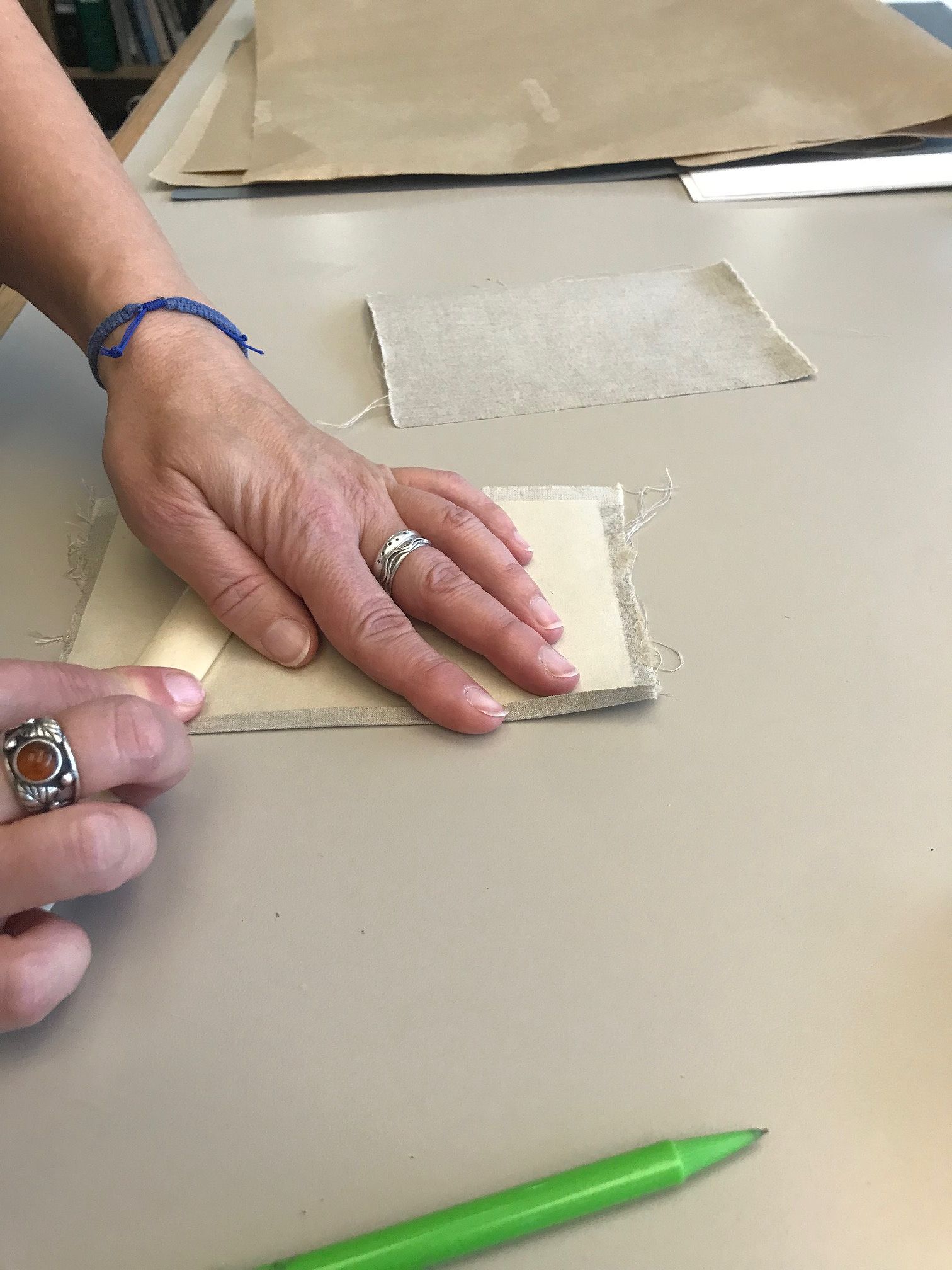 pair of hands, one holding some paper onto a table, and one using a roller on the paper