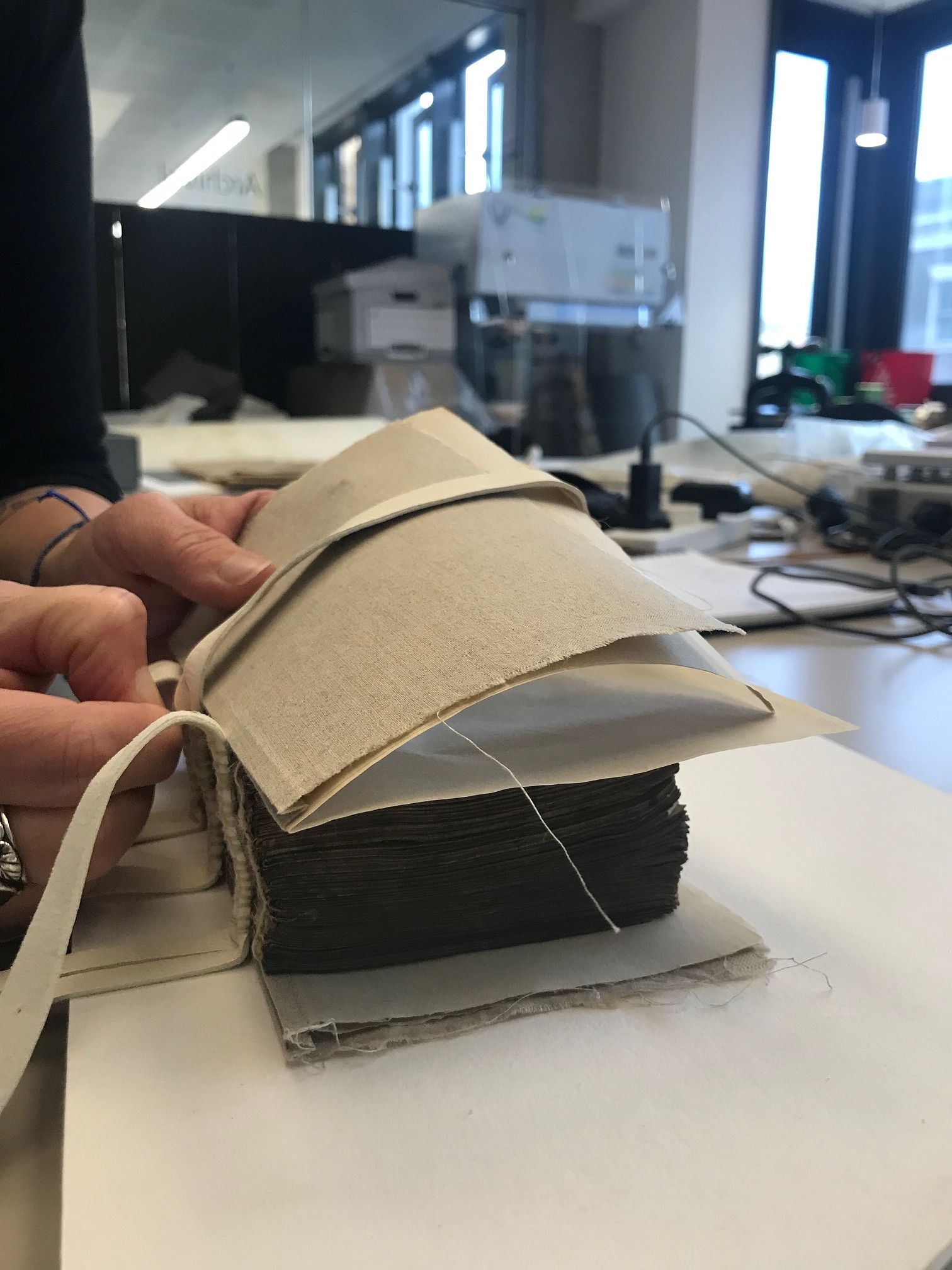 some paper (endpapers) held onto the book with some a piece of material whilst someone binds them together using a handtool