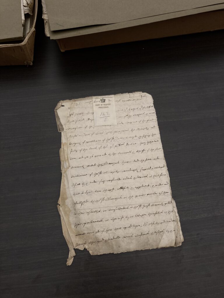 Old piece of paper with handwriting and a label stitched to it with text reading Court of Requests Proceedings 142/5