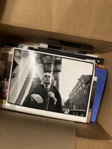 A box of photos with the black and white top photo on show of an old man holding his glasses staring at the camera