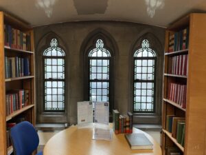 Stone wall with lead lined windows behind a table with bookshelves either side