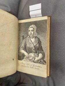 Open book with a drawing of a woman sat in a chair, scarf on her head, holding a rabbit on her lap which is covered by an apron