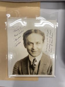 Black and white photo of man, hair parted in middle, smiling with a suit and tie. Signed at the top: to my friend Harry Price, Best wishes Houdini Sept 14/21