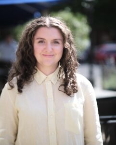 Photo of woman with long curly dark hair and light yellow blouse.